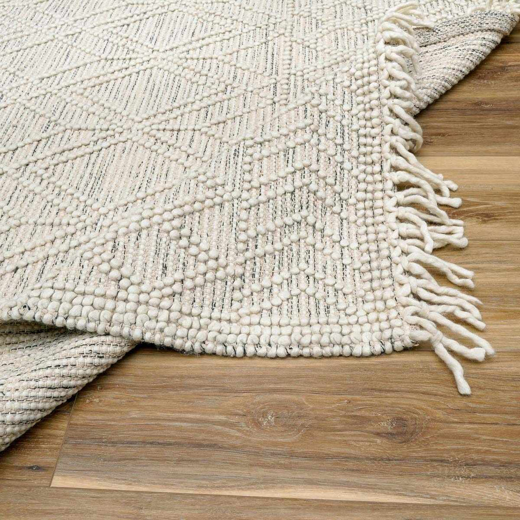 Textured beige rug with fringe on a wooden floor