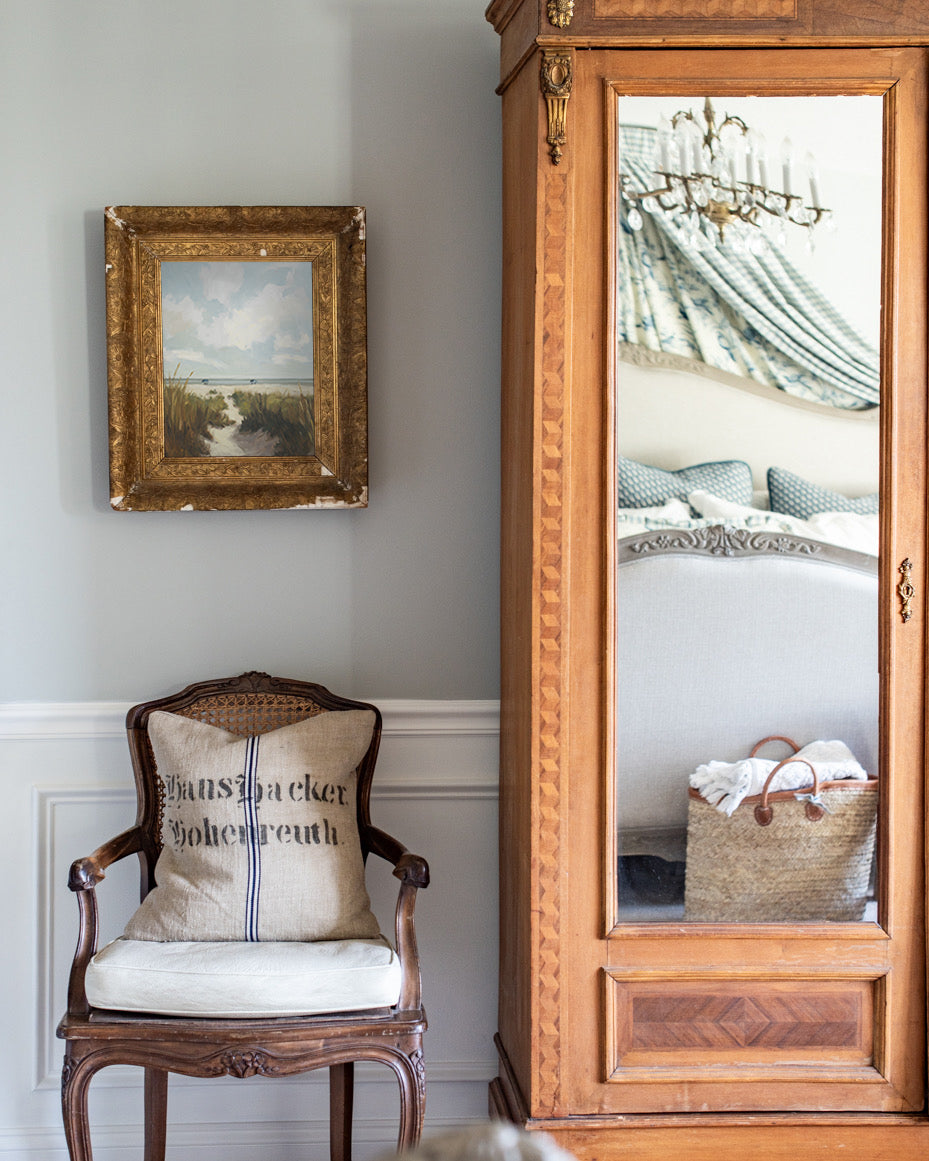 Wooden armchair with a cushion, ornate mirror, and framed picture on a wall.