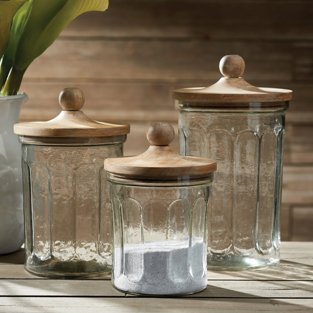 Three glass jars with wooden lids on a wooden surface.