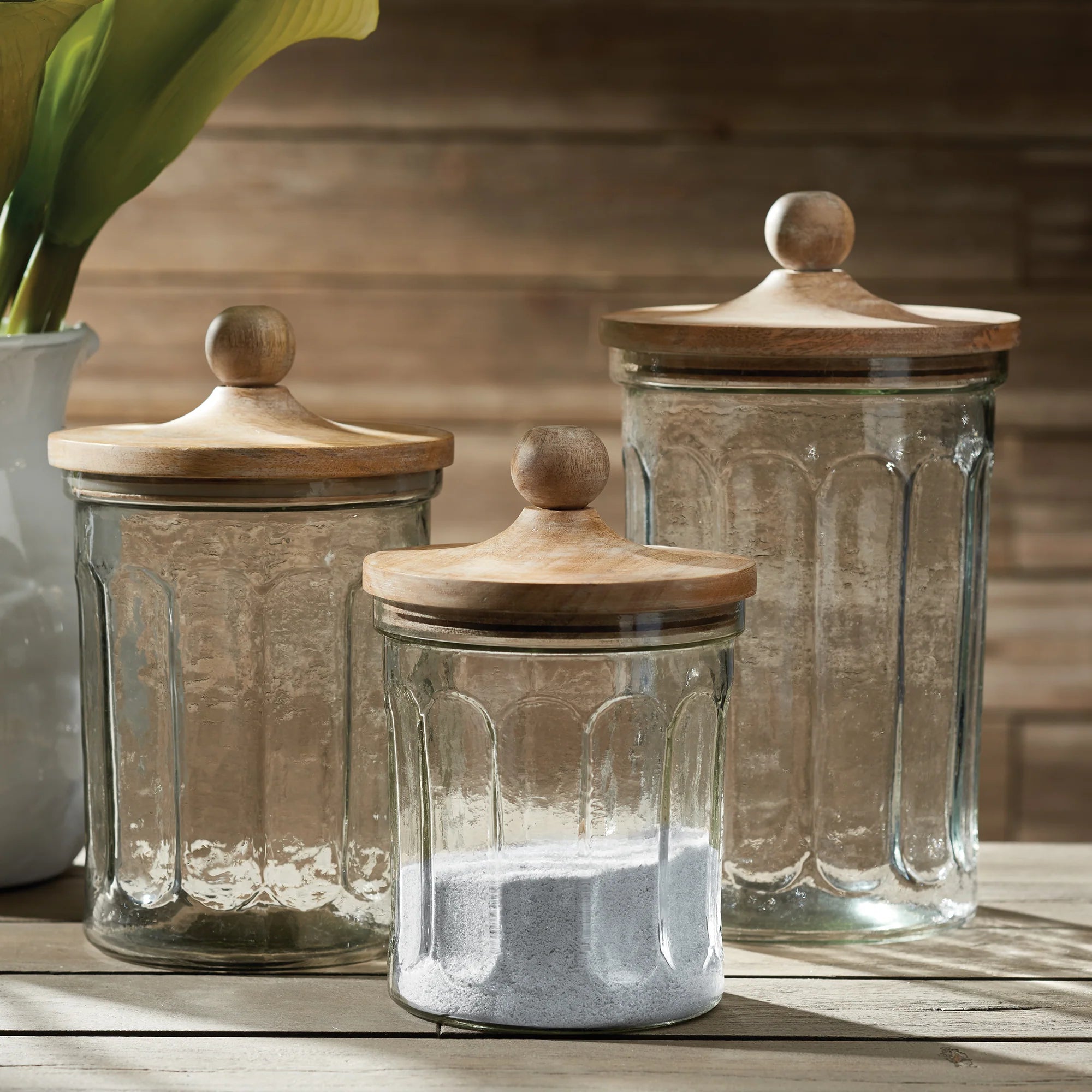 Three glass jars with wooden lids on a wooden surface.