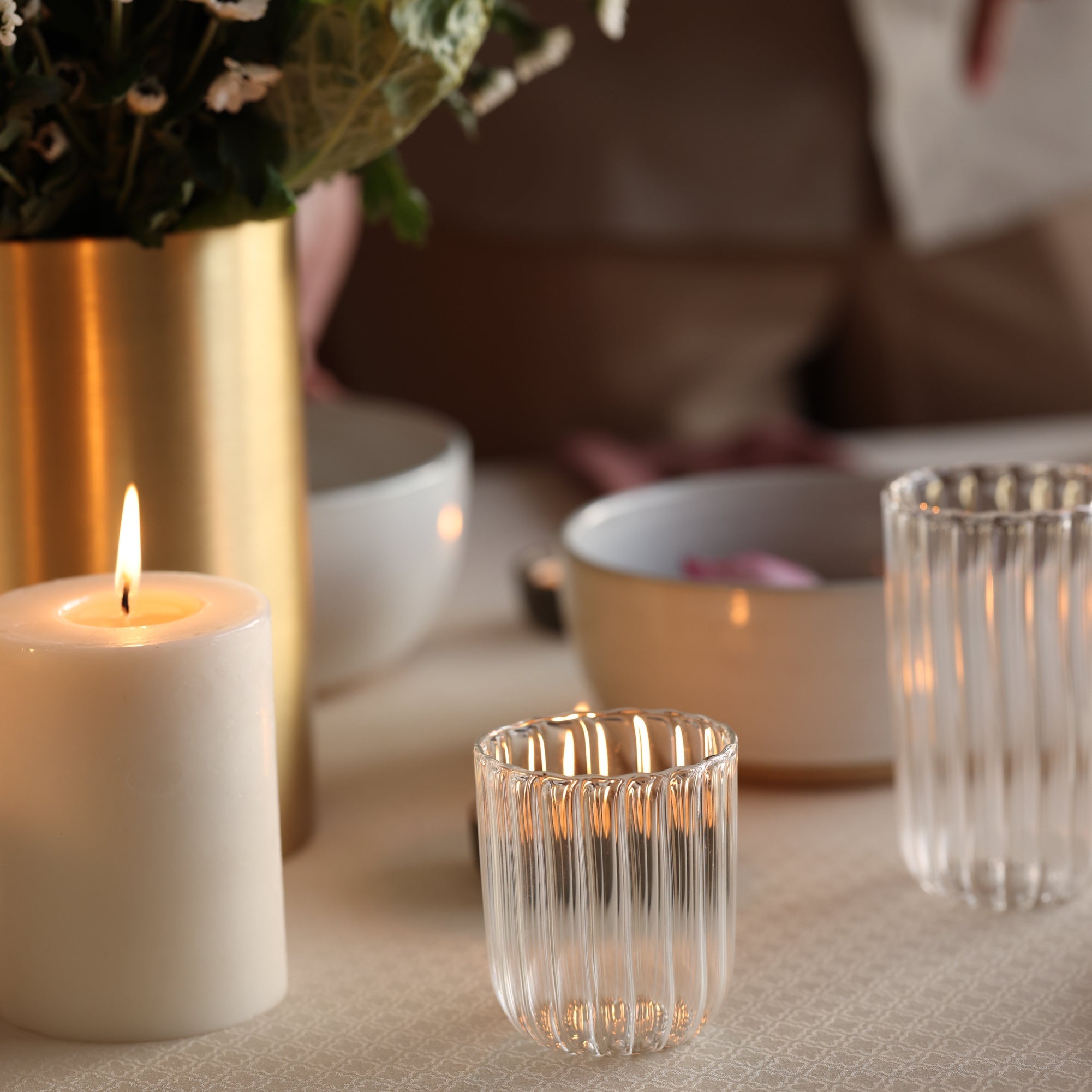 Candlelit table setting with a vase, bowls, and glasses on a soft surface.