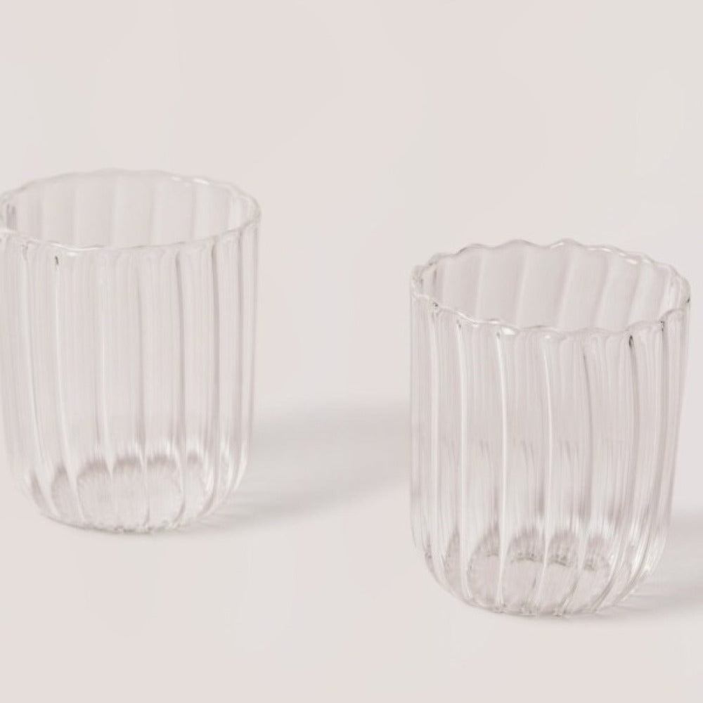 Two clear glass tumblers with ribbed design on a light gray background