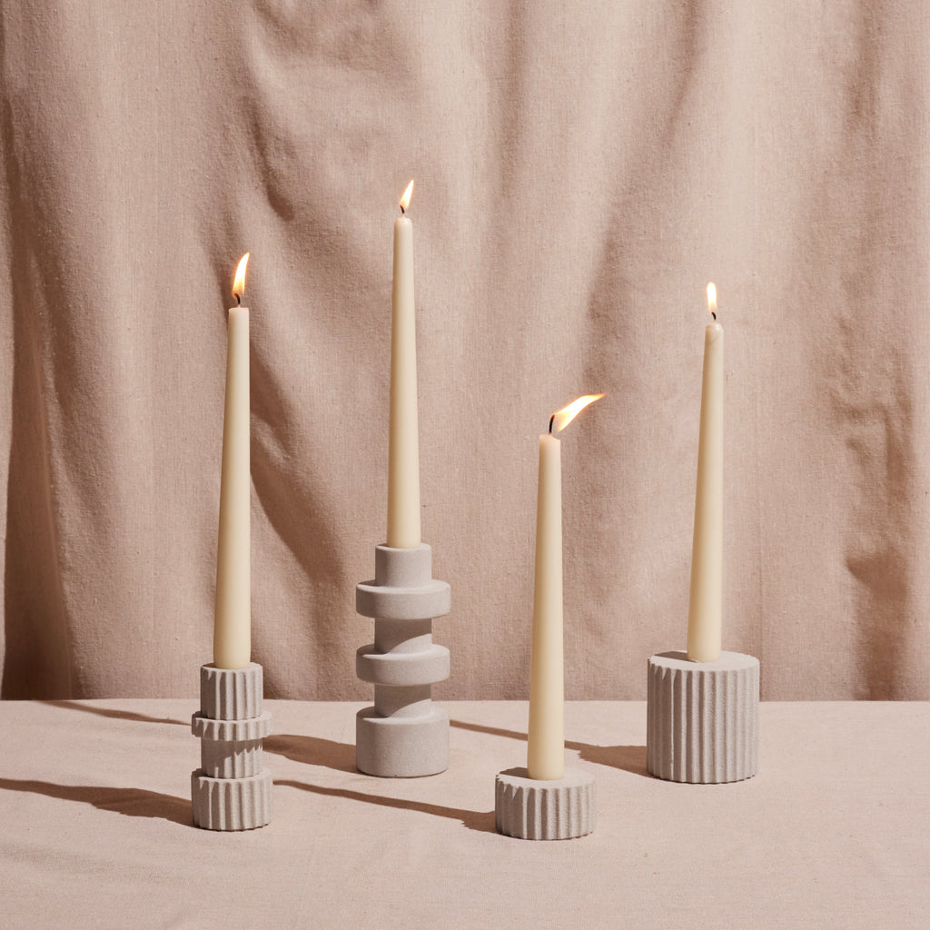 Four candles in decorative holders against a beige curtain background