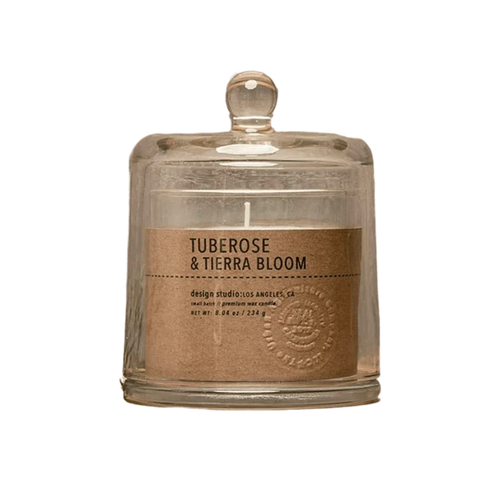 A glass jar candle with a clear glass dome lid and a kraft paper label reading 'TUBEROSE & TIERRA BLOOM' by design studios anicut, on a white background.