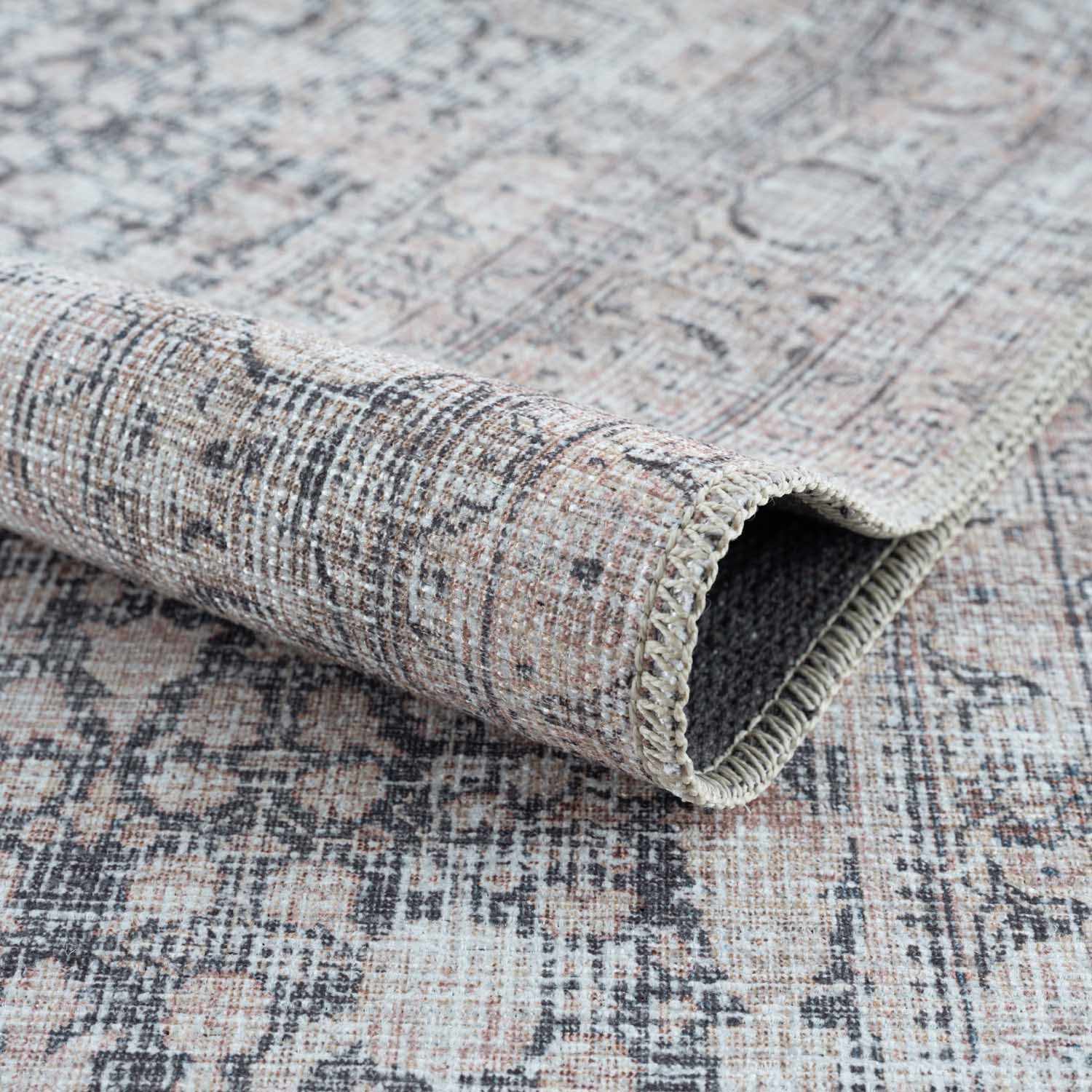 Textured rug with a patterned design, partially rolled up on a matching surface.