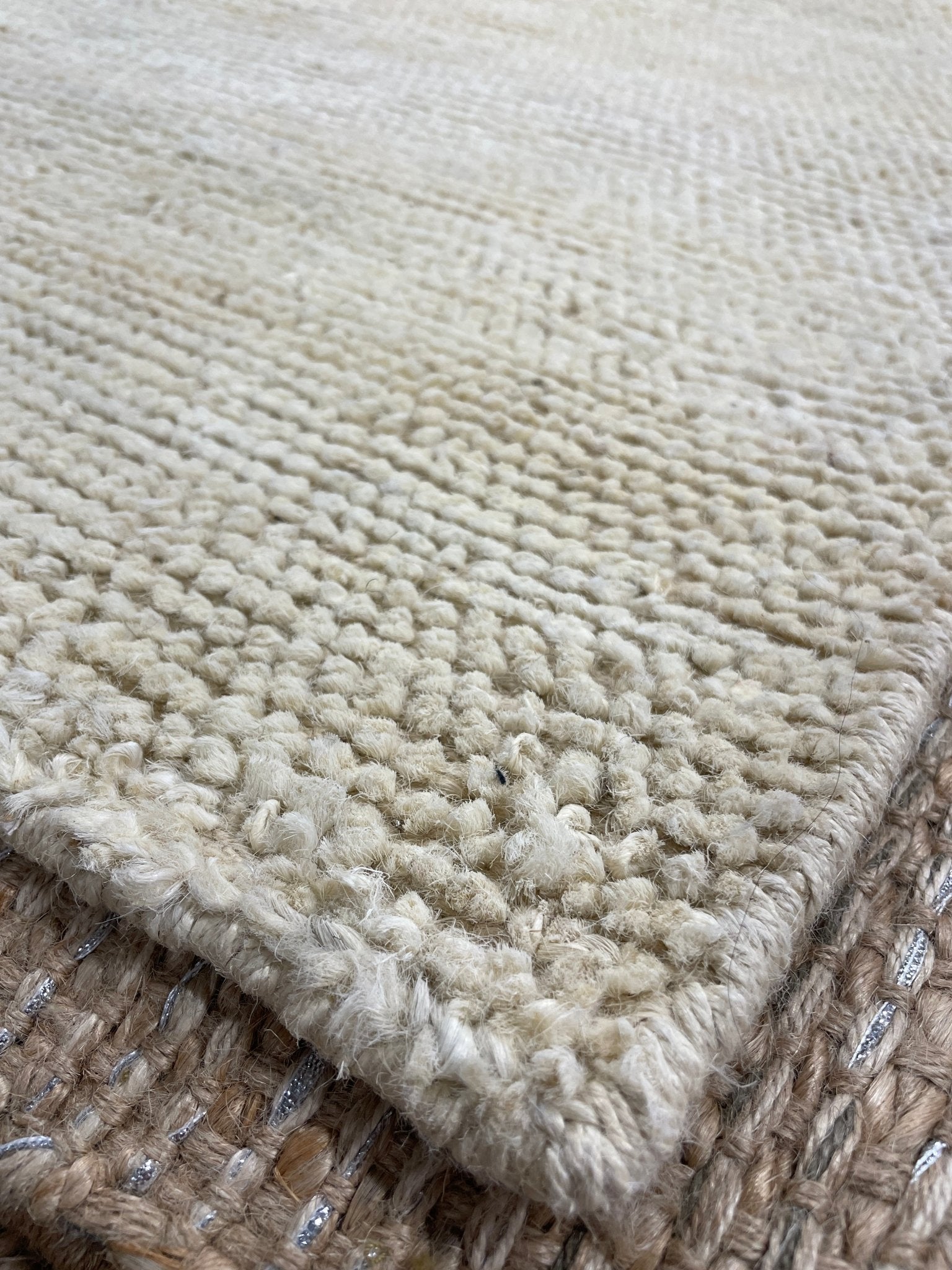 Close-up of a chunky, textured off-white rug with a raised border, layered over a woven brown and beige jute surface.