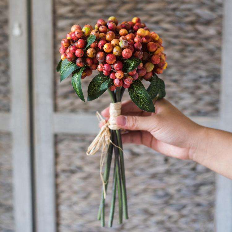 Hand holding a bouquet of red and green berries against a neutral background
