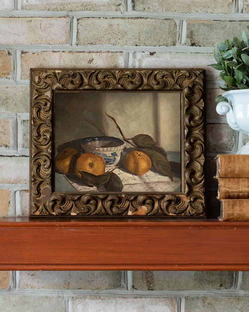 Framed still life painting on a wooden surface with a brick wall background