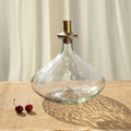 Clear glass decanter with a gold stopper on a textured surface with two cherries.