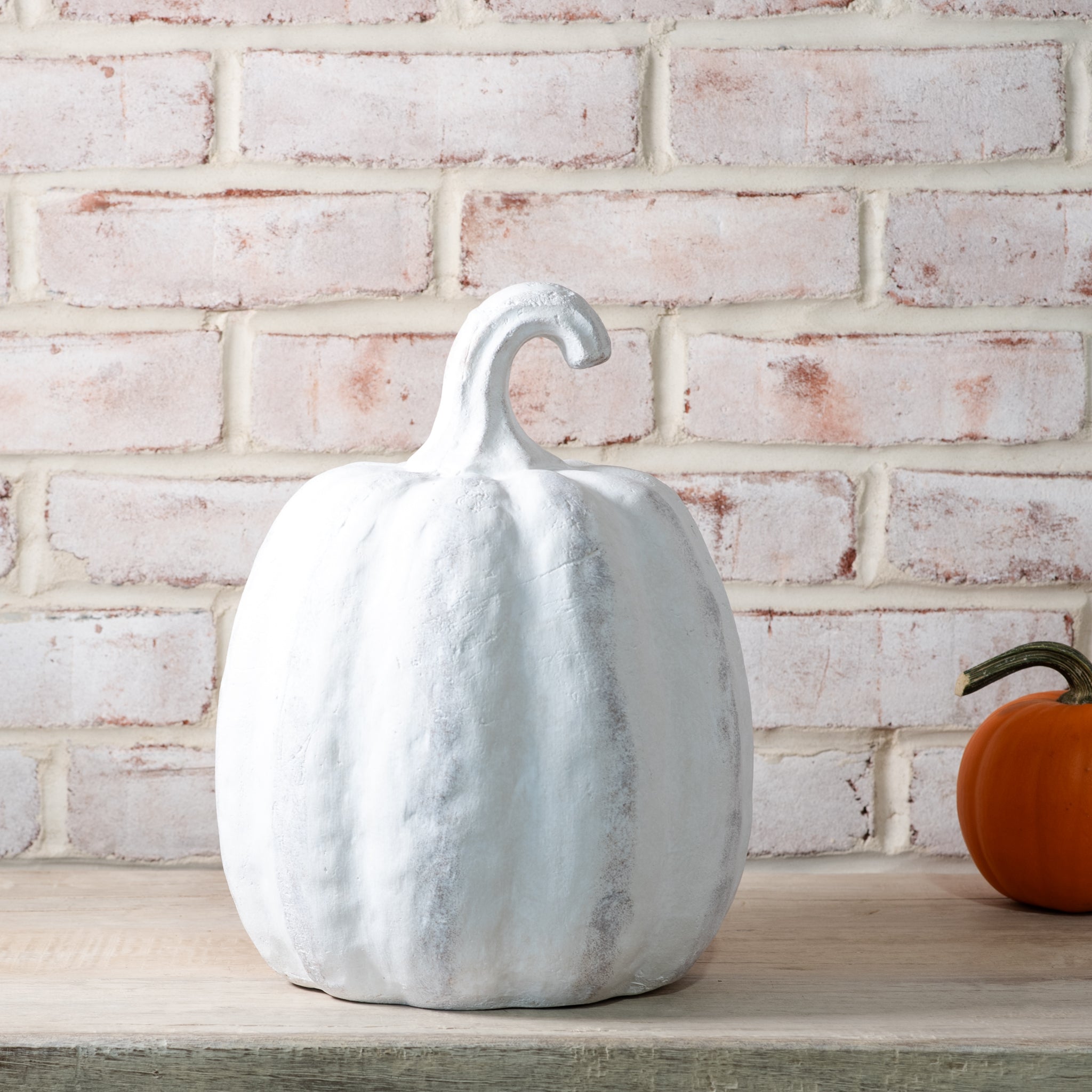 White decorative pumpkin on a wooden surface with a brick wall background