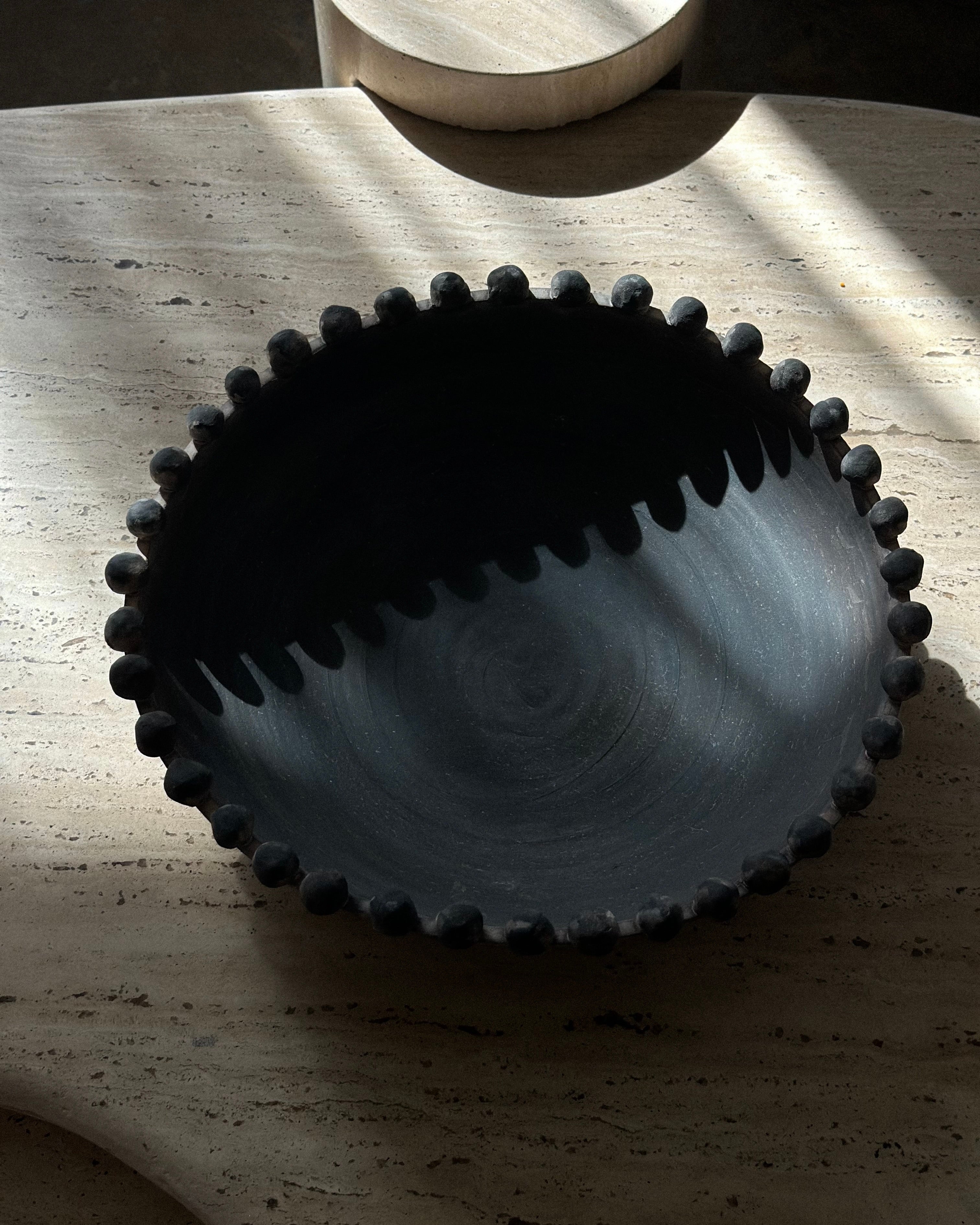 Black ceramic bowl with textured rim on a wooden surface