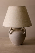 Table lamp with a textured beige shade and ceramic base on a wooden surface.