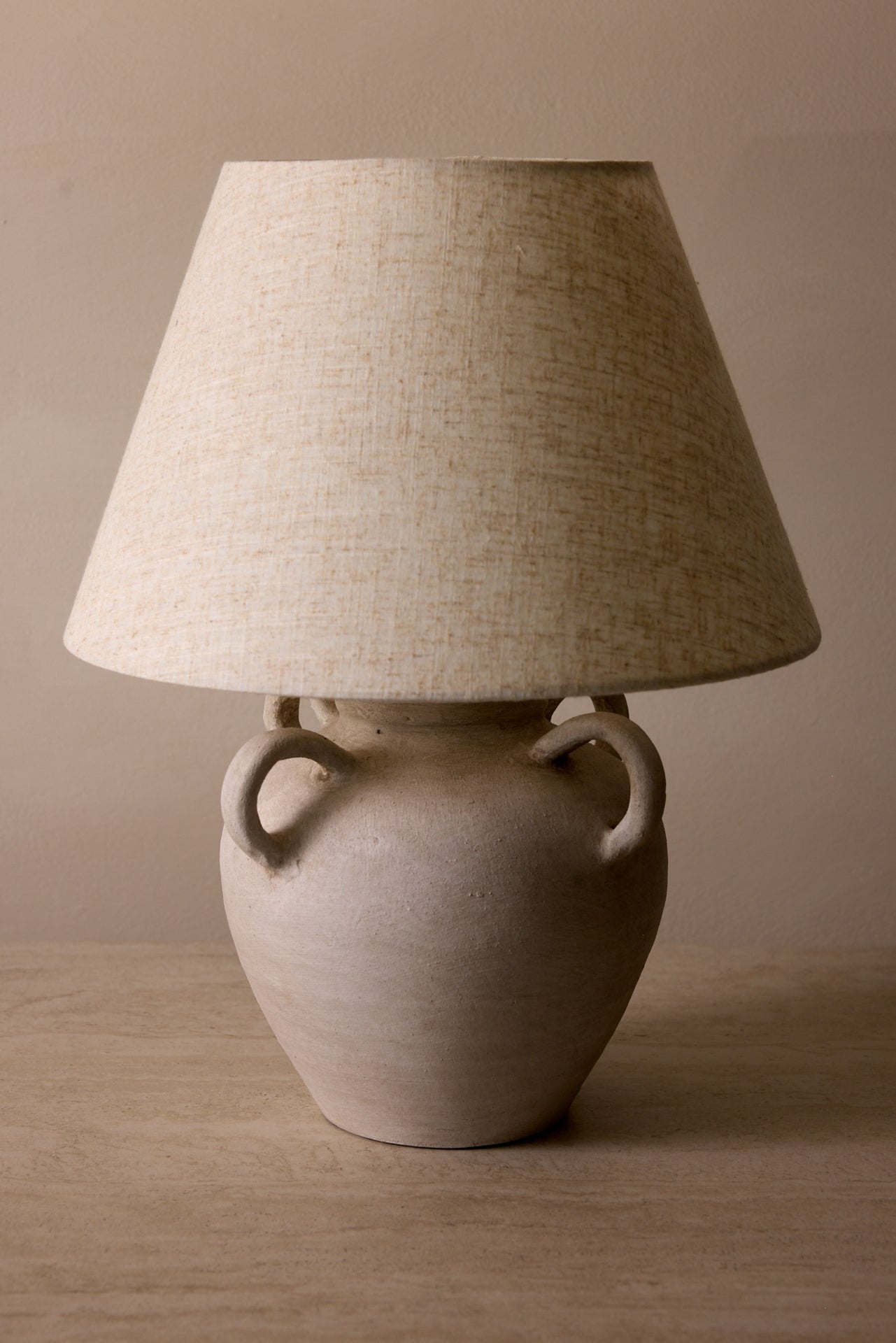 Table lamp with a textured beige shade and ceramic base on a wooden surface.