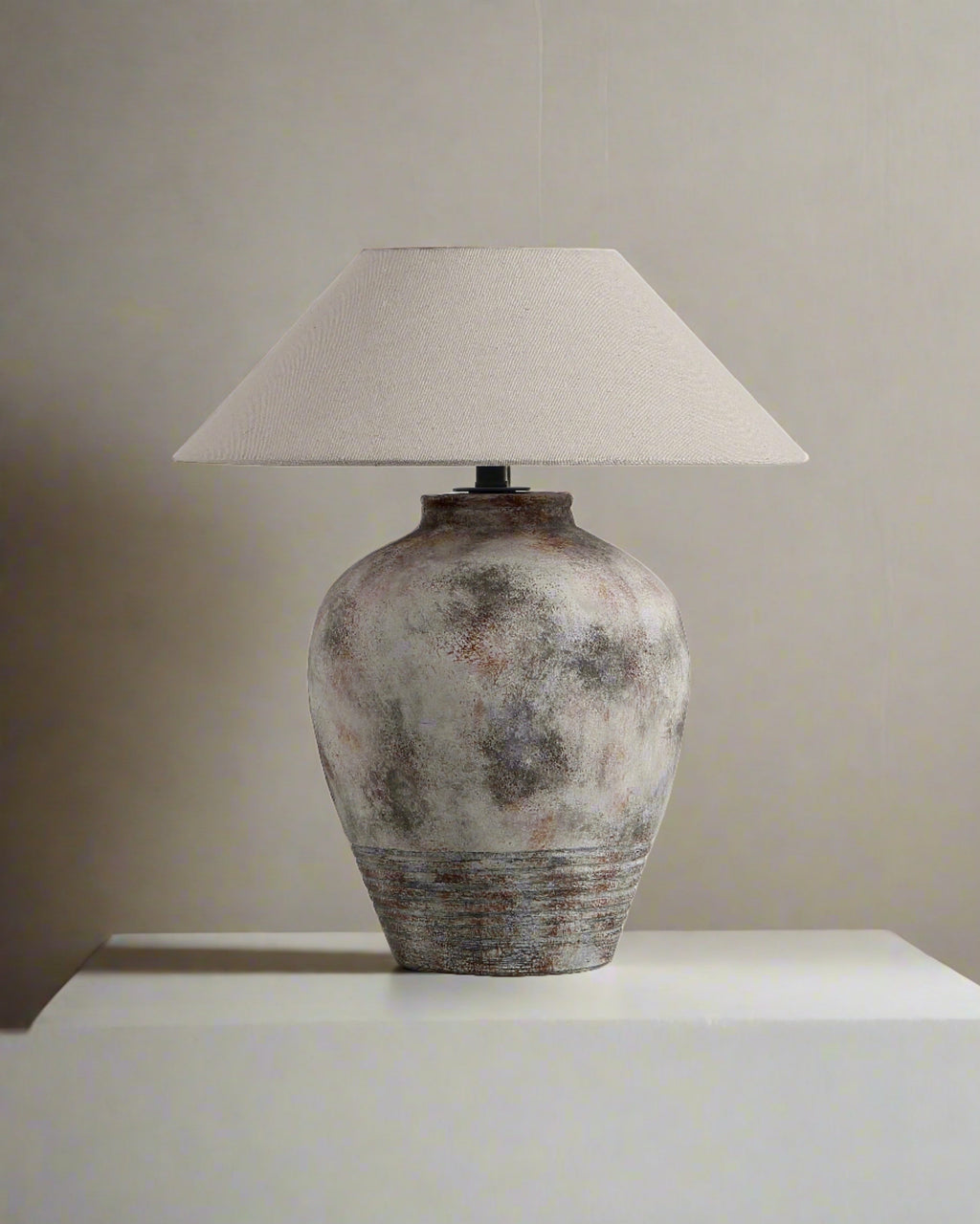 Table lamp with textured ceramic base and white lampshade on a neutral background