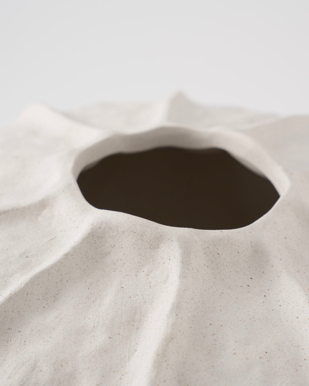 Close-up of a textured ceramic vase with a dark interior on a light background