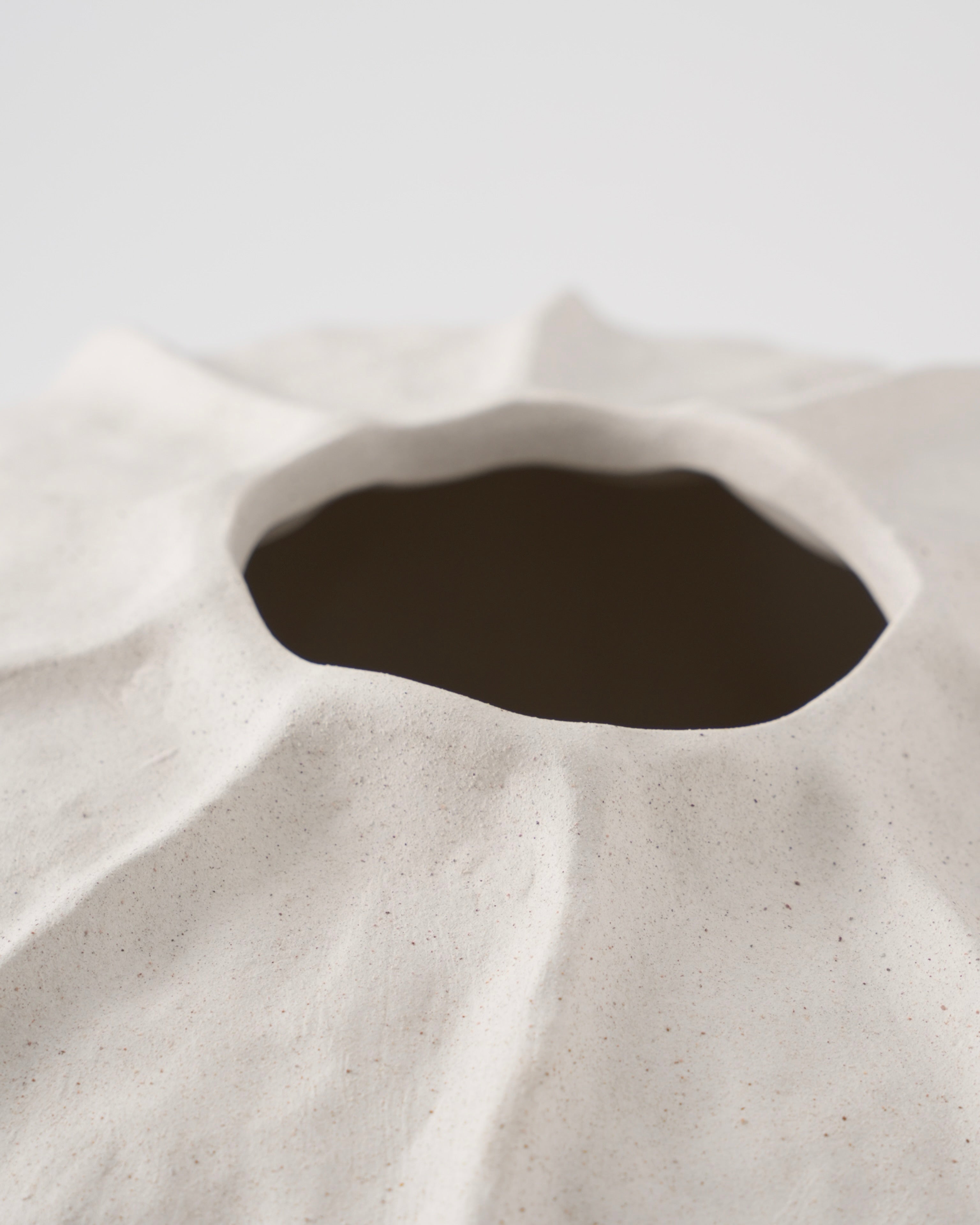 Close-up of a textured ceramic vase with a dark interior on a light background