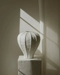 White textured vase on a pedestal against a wall with light shadows