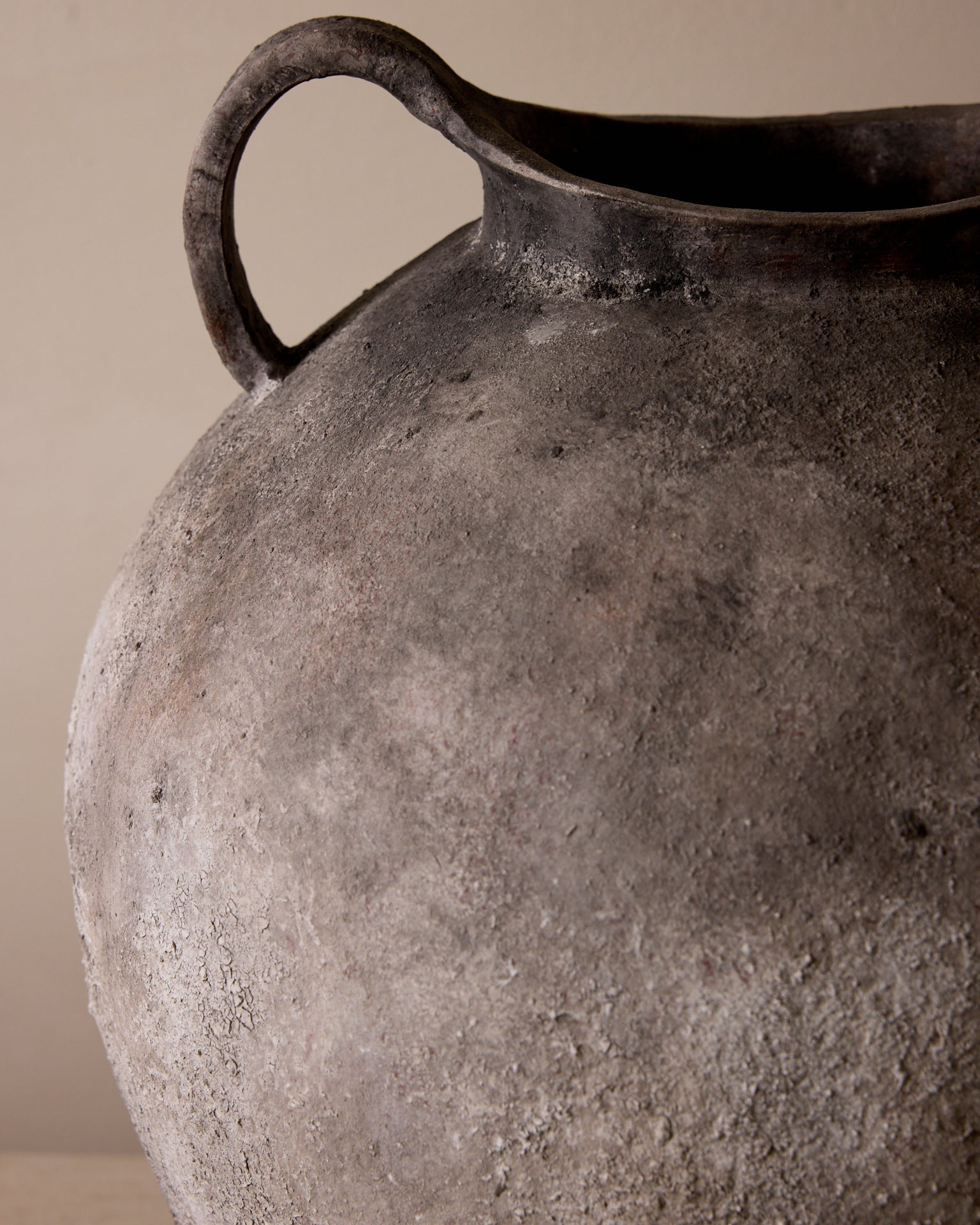 Close-up of a textured ceramic vase with a handle on a beige background