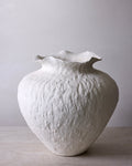 White textured vase on a light wooden surface with a plain background
