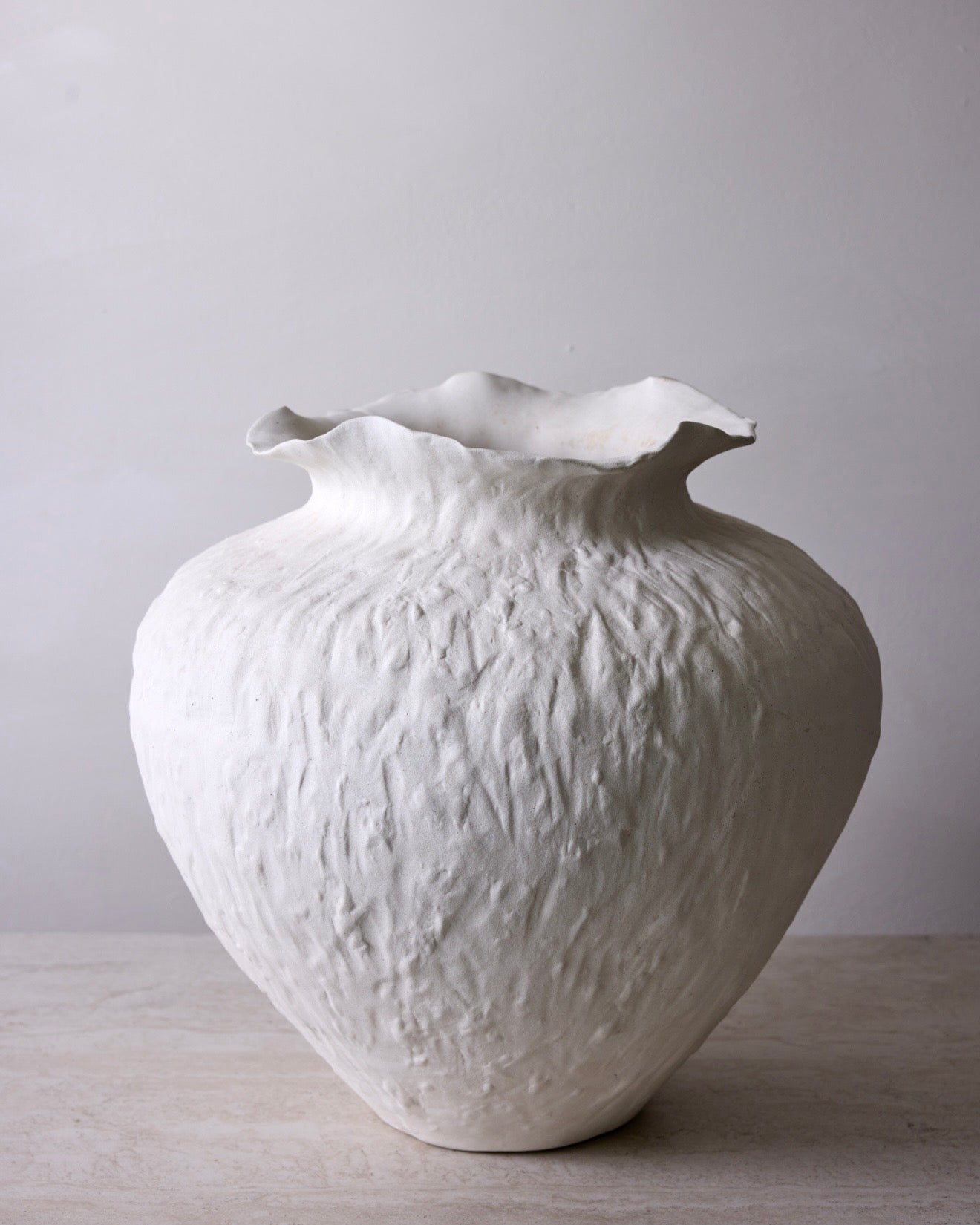 White textured vase on a light wooden surface with a plain background