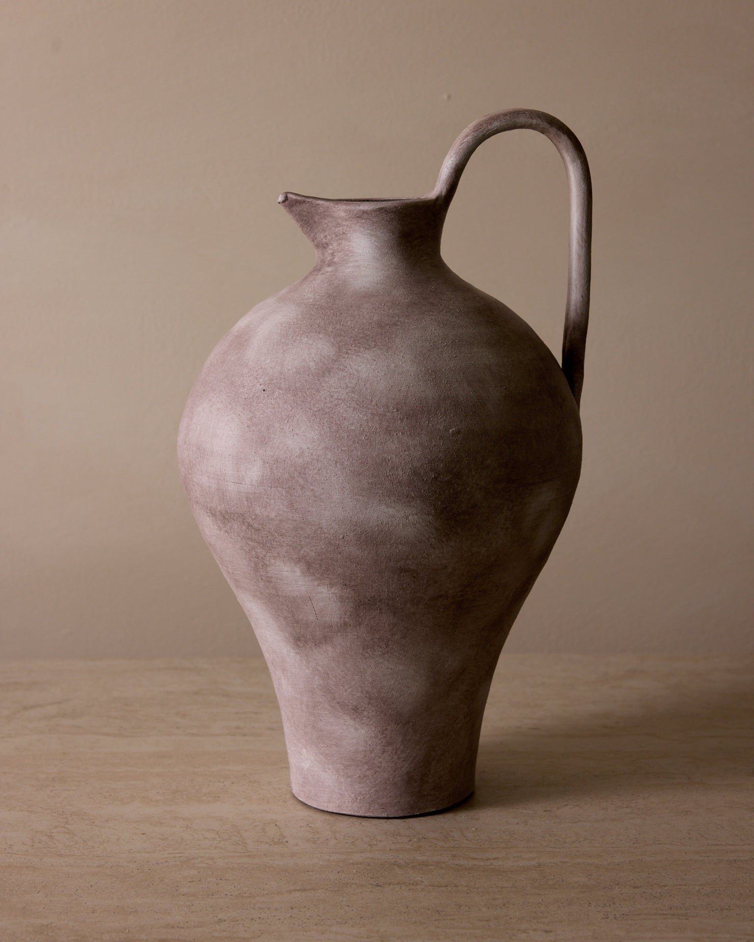 Brown ceramic pitcher on a beige surface with a beige background