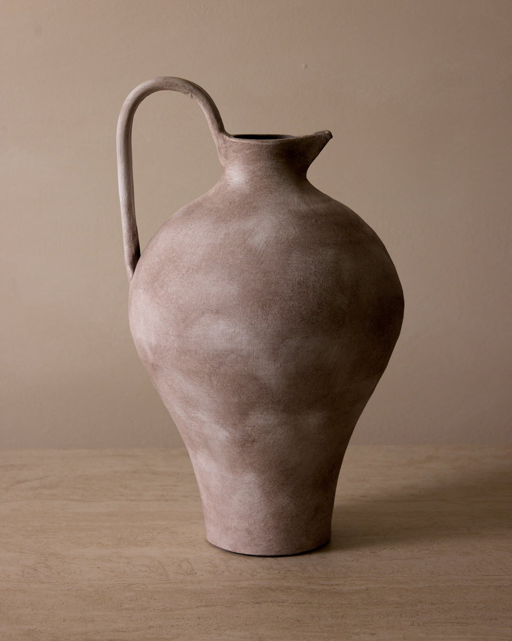 Brown ceramic pitcher on a wooden surface with a beige background