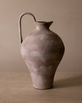 Brown ceramic pitcher on a wooden surface with a beige background