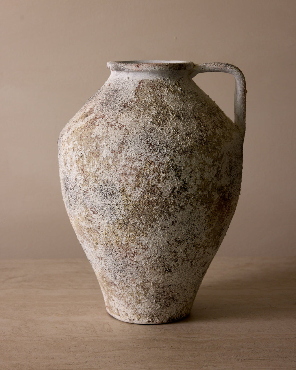 Vintage ceramic pitcher with a textured surface on a beige background