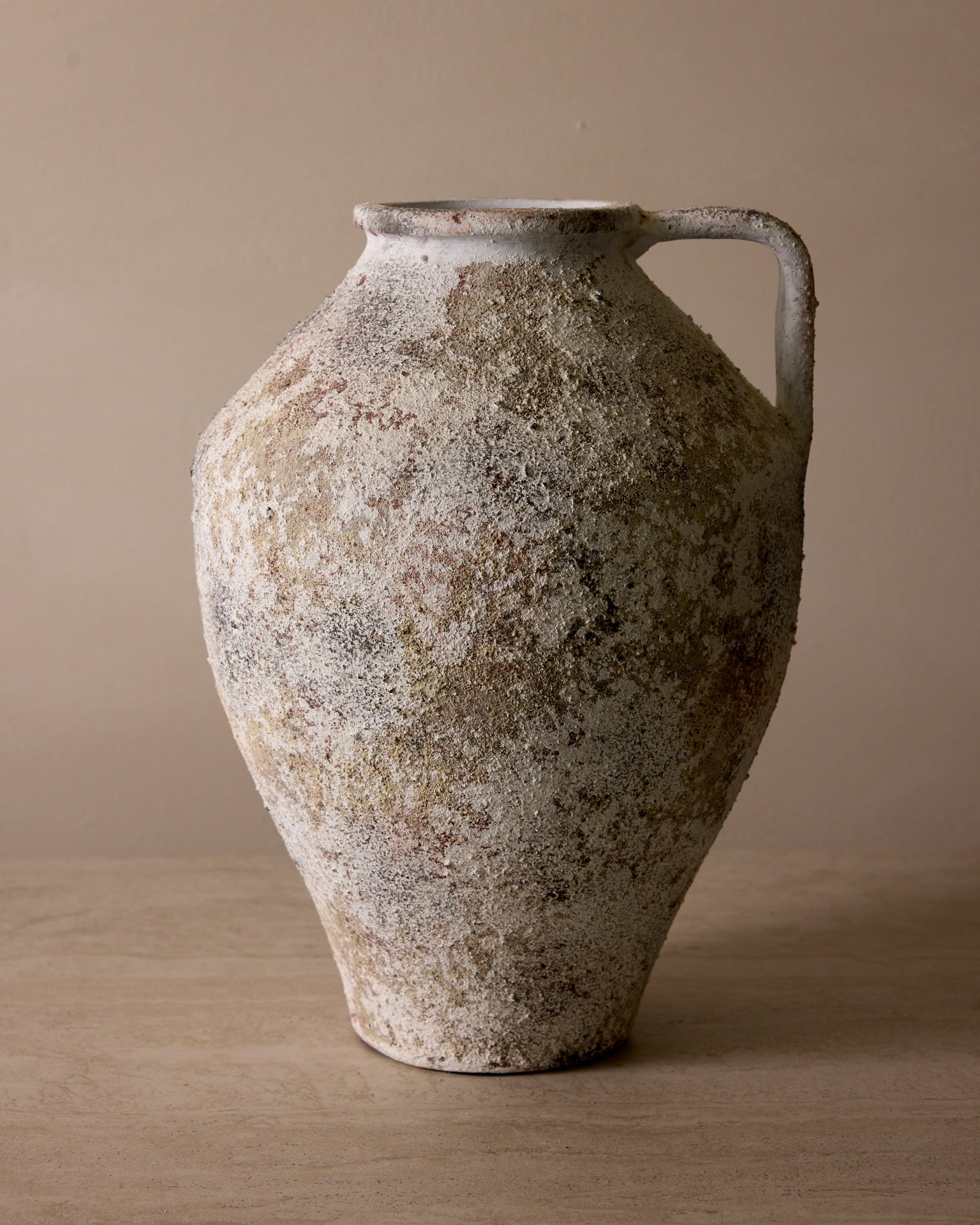 Vintage ceramic pitcher with a textured surface on a beige background