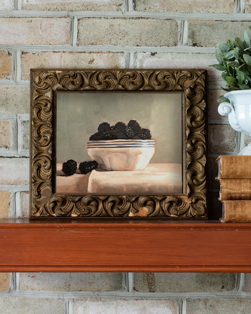 Framed painting on a wooden shelf against a brick wall