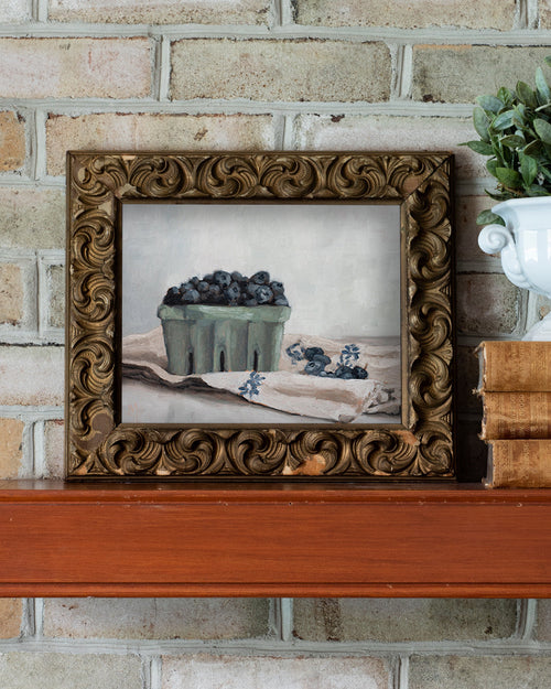 Framed still life painting of blueberries on a wooden shelf against a brick wall.