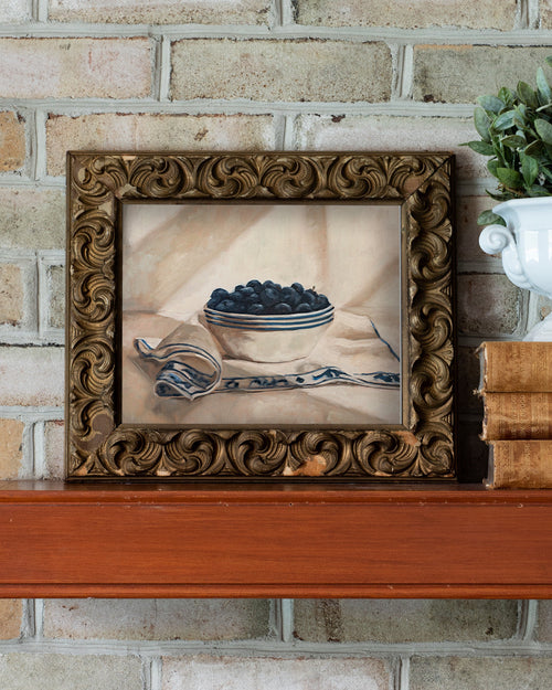 Framed still life painting on a wooden surface with a brick wall background