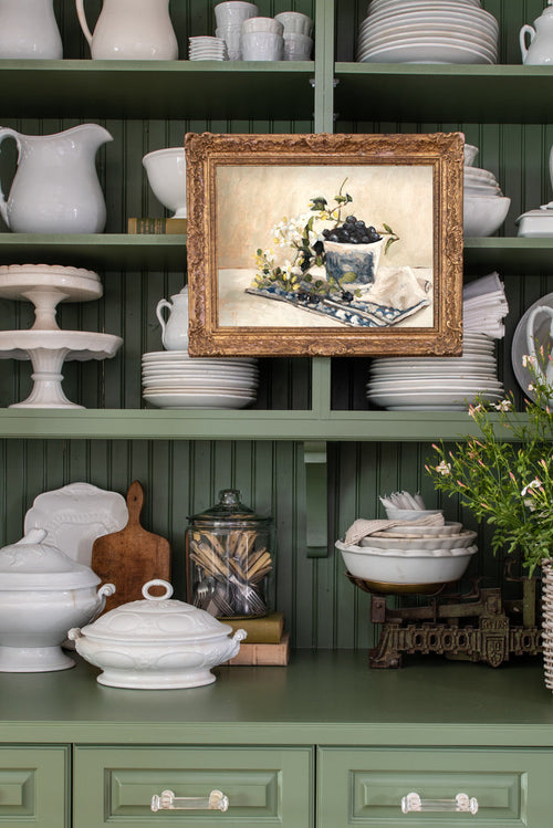 Green kitchen shelf with white ceramic items and a framed picture.