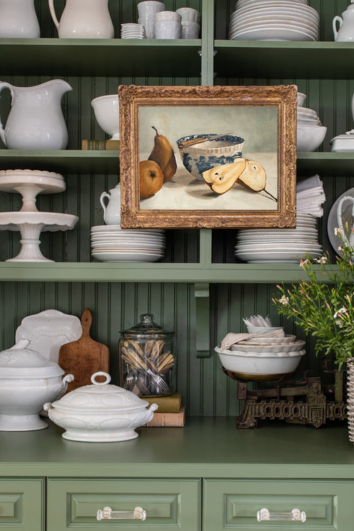 Green kitchen shelf with various ceramic items and a framed still life painting.