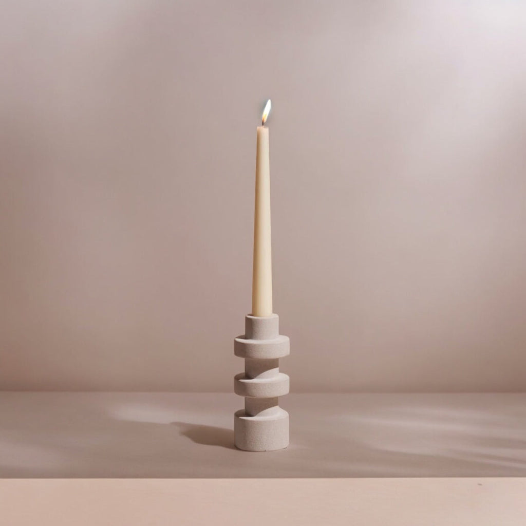 Ceramic candle holder with a lit candle on a neutral background