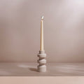 Ceramic candle holder with a lit candle on a neutral background