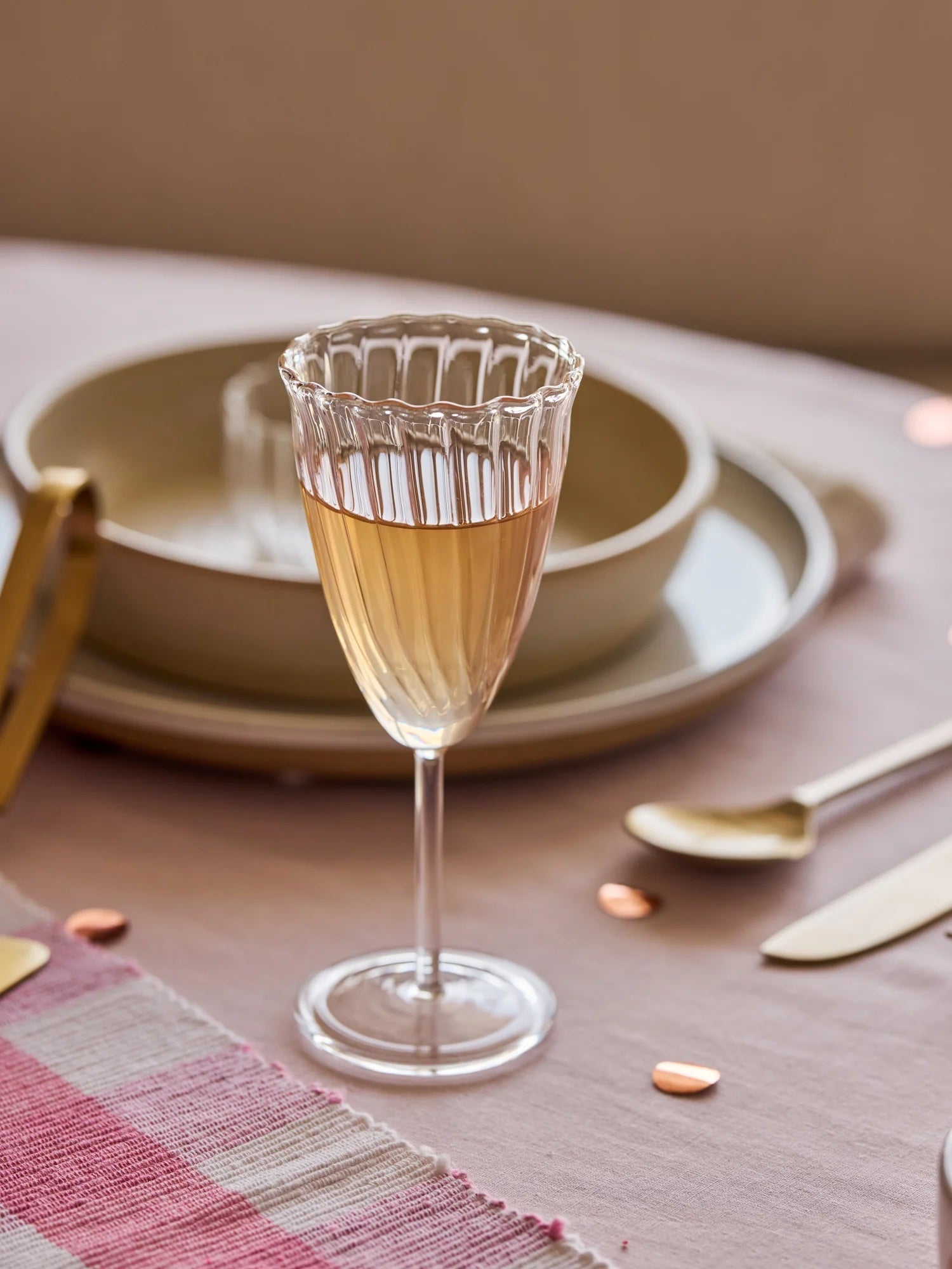 Glass of champagne on a table setting with plates and cutlery.