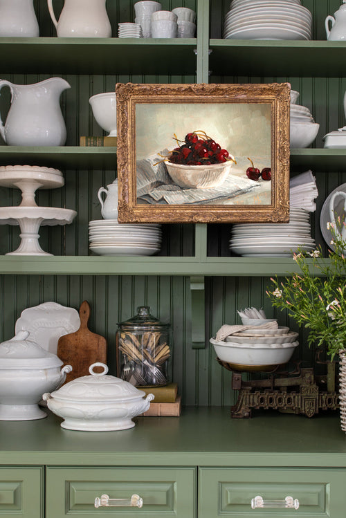 Green kitchen shelf with white ceramic items and a framed painting of cherries.