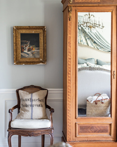 Wooden chair with a cushion and decorative pillow in a room with a large mirror and framed picture on the wall.