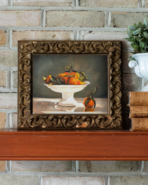 Framed still life painting on a wooden surface with a brick wall background