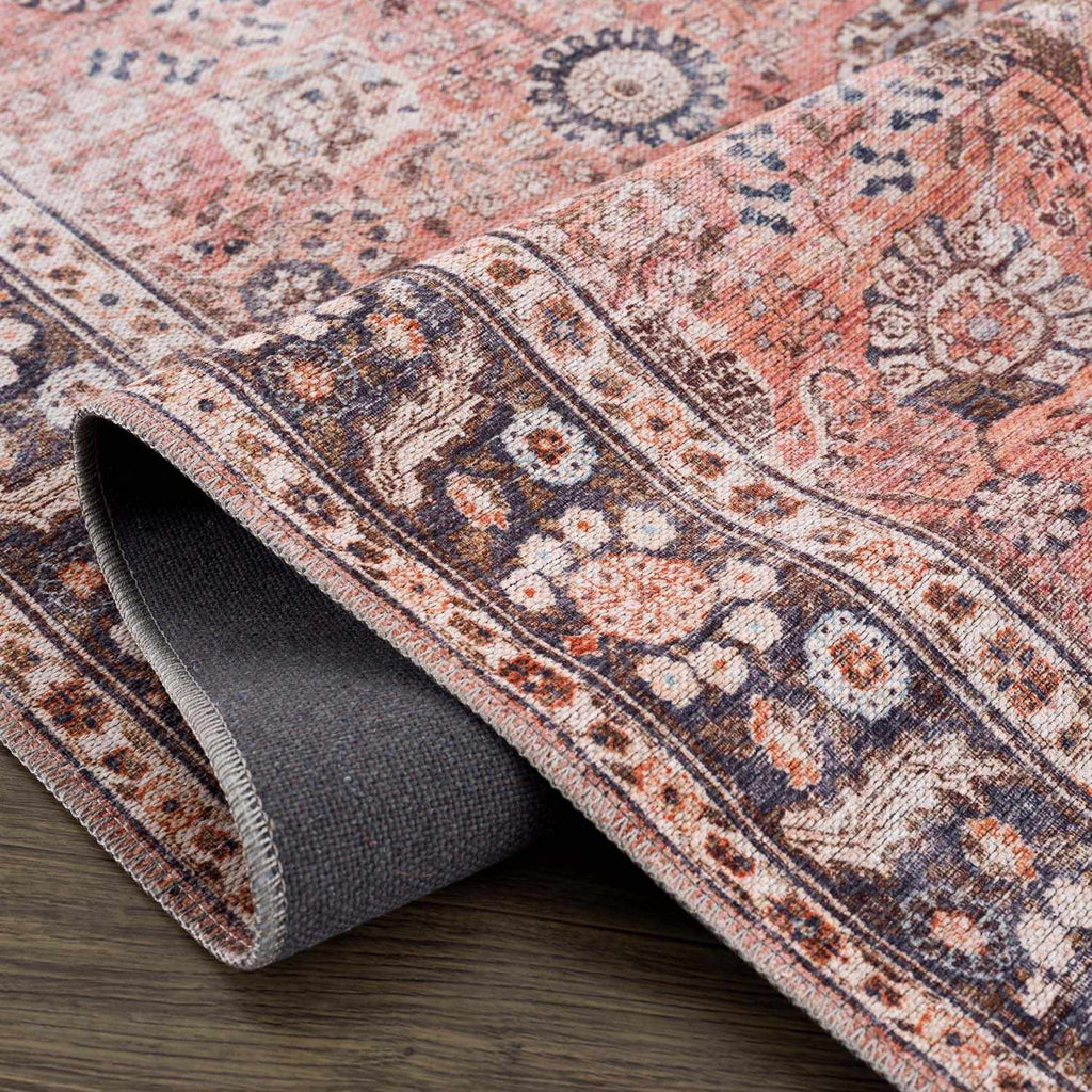 Close-up of a patterned rug with a roll of rug on a wooden floor.