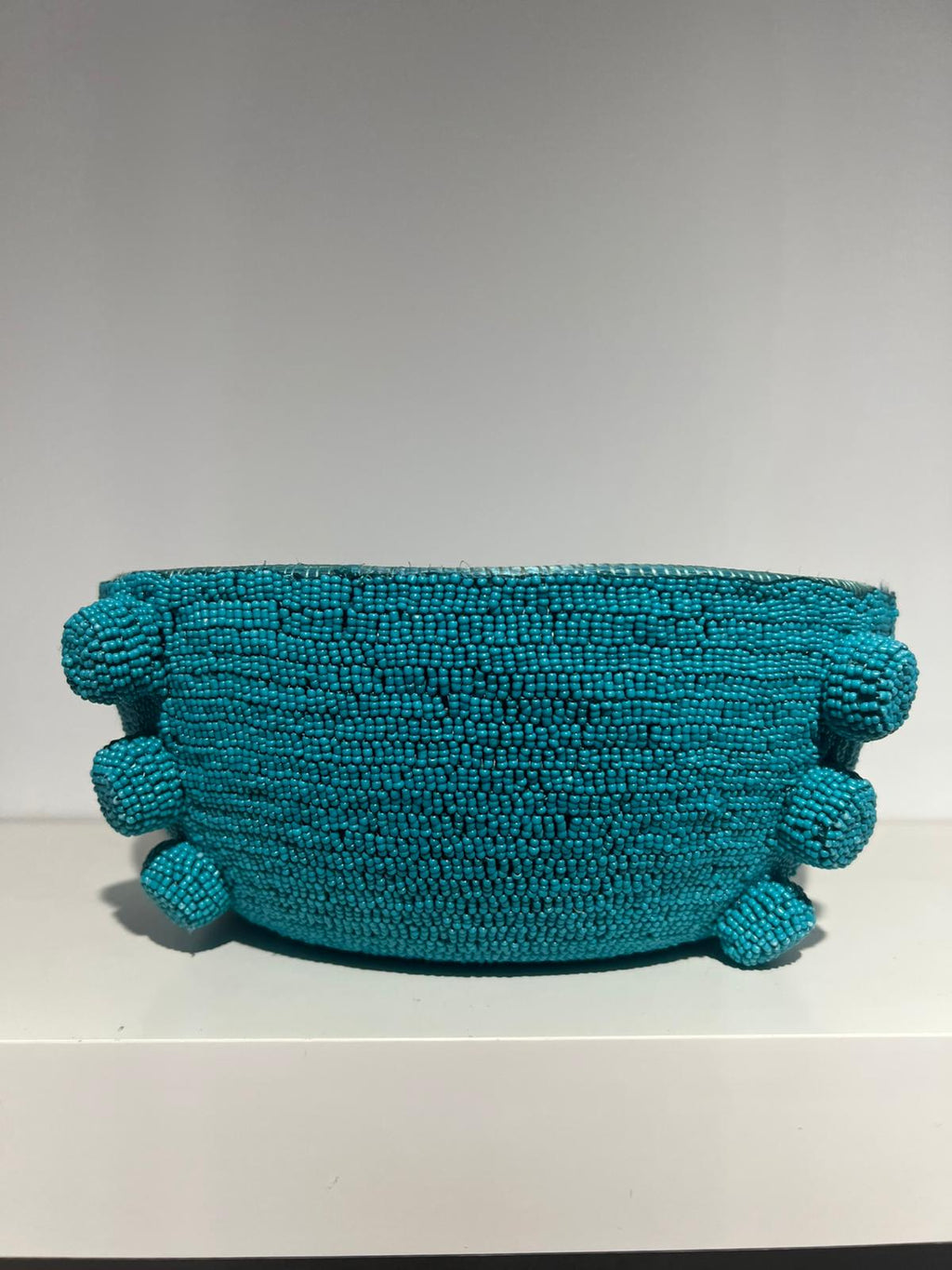 Turquoise beaded clutch bag on a white surface with a gray background
