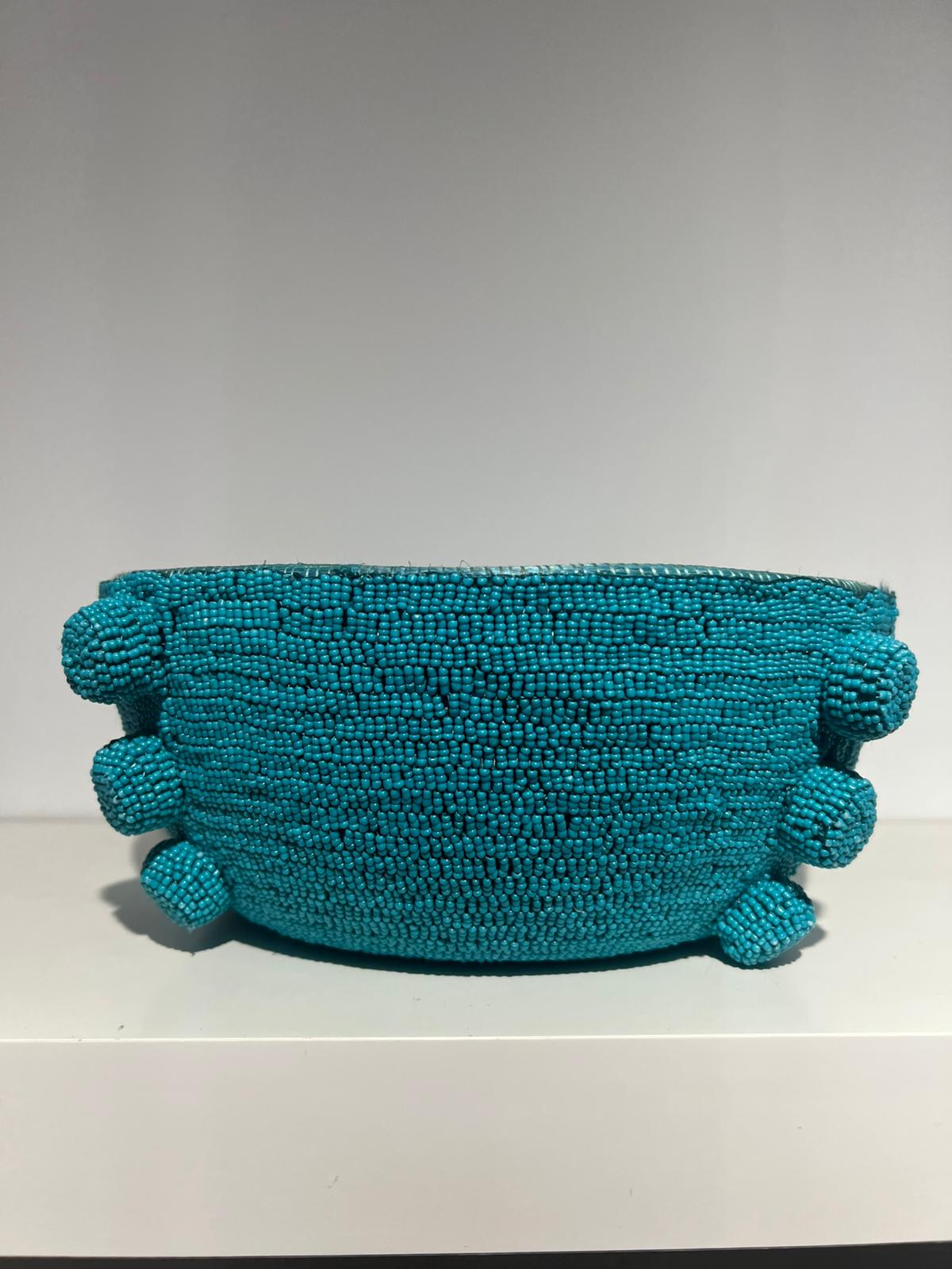 Turquoise beaded clutch bag on a white surface with a gray background
