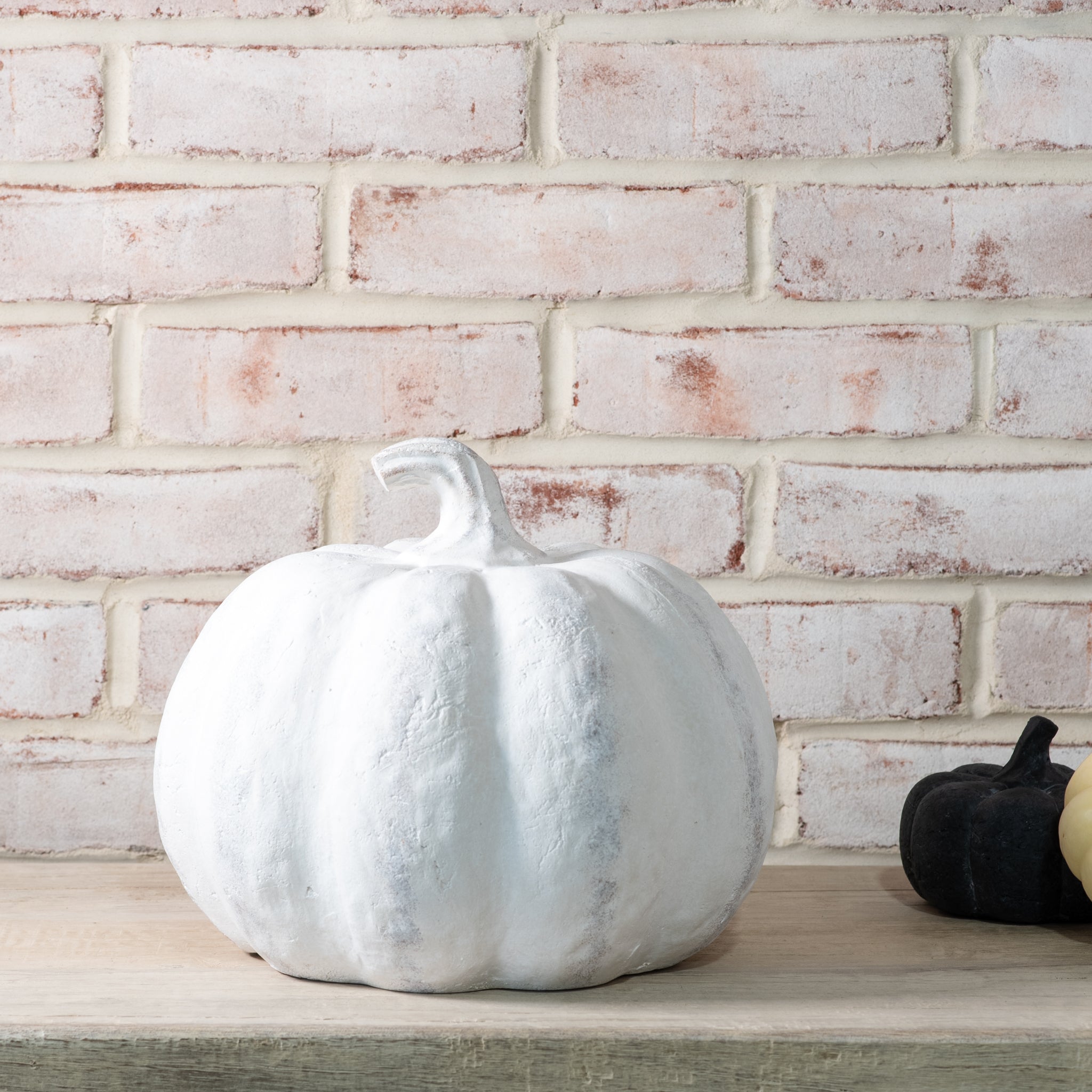 White textured pumpkin on a wooden surface with a white brick wall background