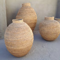 Three woven vases of different sizes against a plain wall.