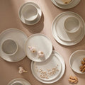 White ceramic plates and bowls on a beige surface with garlic and nuts.