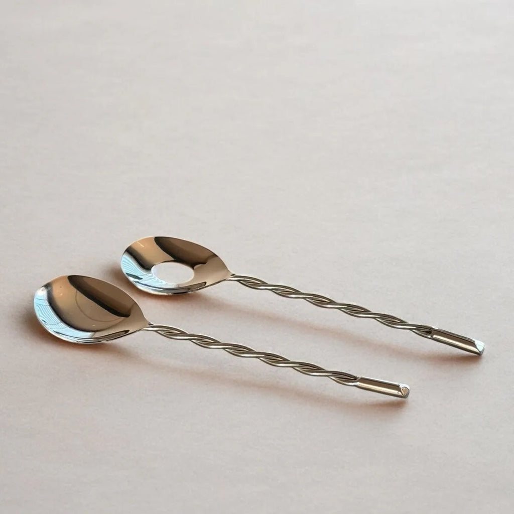 Two silver spoons with twisted handles on a light pink background
