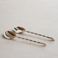Two silver spoons with twisted handles on a light pink background