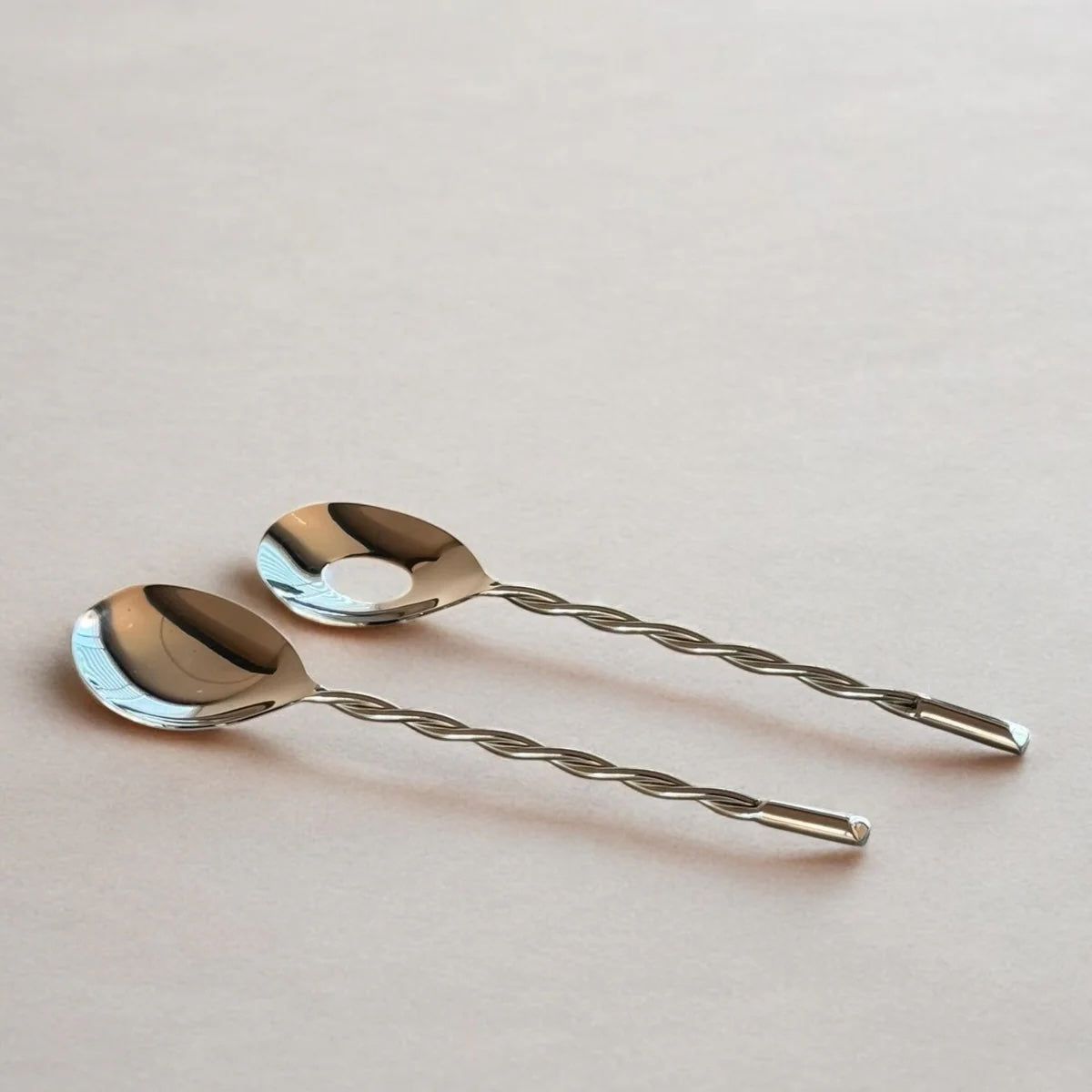 Two silver spoons with twisted handles on a light pink background