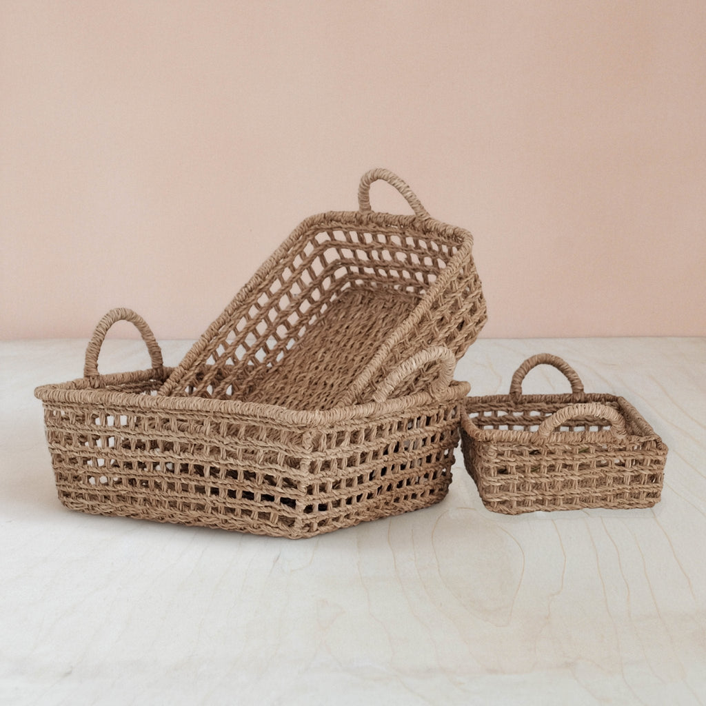 Three woven baskets of different sizes on a light surface with a soft pink background